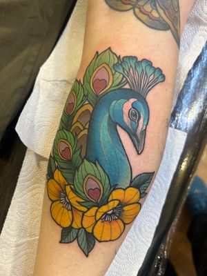 Vibrant neo-traditional tattoo of a peacock surrounded by traditional flowers, expertly done by Lawrence Canham.