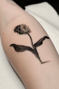 A contemporary surreal realism tattoo combining a pixelated bloom with realistic leaves and stem. This black and grey micro realism piece merges digital distortion with organic beauty.