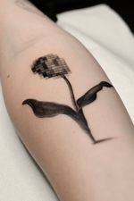 A contemporary surreal realism tattoo combining a pixelated bloom with realistic leaves and stem. This black and grey micro realism piece merges digital distortion with organic beauty.