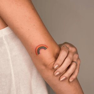 A delicate watercolor tattoo featuring a vibrant rainbow, created by artist Larissa.