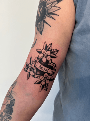 A traditional black and gray tattoo by Kayleigh Cole featuring a heart with the word 'mom' in a banner, perfect for honoring a special mother figure.