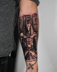 A powerful black and grey realism tattoo depicting Anubis, the ancient Egyptian god of the afterlife, guarding the pyramids. Detailed hieroglyphics and fine shading bring depth and mystique to the piece, symbolising protection, judgment, and the journey beyond life. Tattoo by London artist Roudolf Dimov.