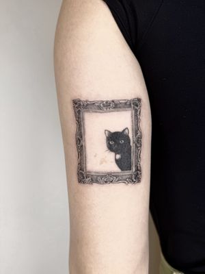 A black and gray micro-realism tattoo of a cat framed in intricate filigree, resembling a painting. By artist Winnie Shwe.