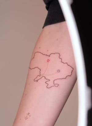 Capture the love for travel and home with Maria's fine line illustrative tattoo featuring a heart and map motif.