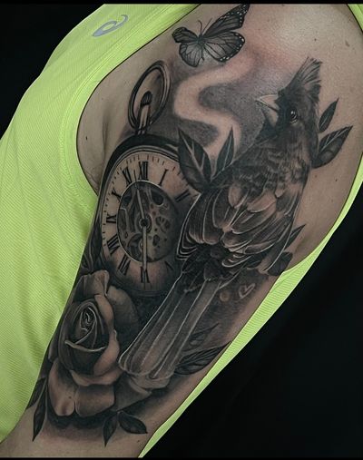 This black and gray realism tattoo by Cara Hayward features a detailed butterfly, rose, red robin, and a watch and clock, creating a beautiful and timeless nature-inspired design.