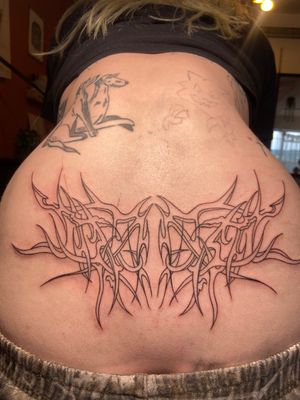 Get a unique fusion of neotribal and tramp stamp styles with this stunning lettering tattoo by the talented artist Beth Farbrother.