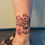 Monk sat writing at a scriptorium desk, in a blended woodcut and etching style, on the ankle.