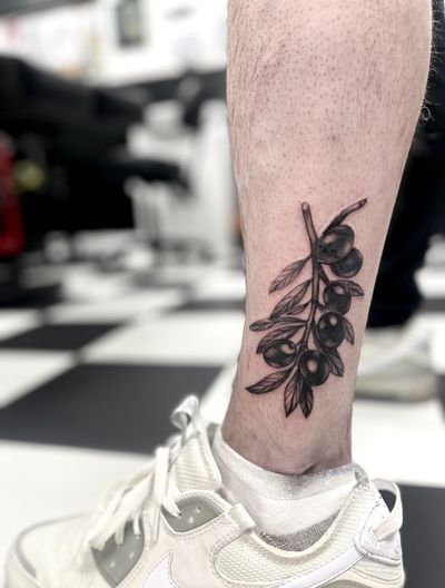 Detailed black and gray tattoo of an olive tree branch by Cara Hayward.