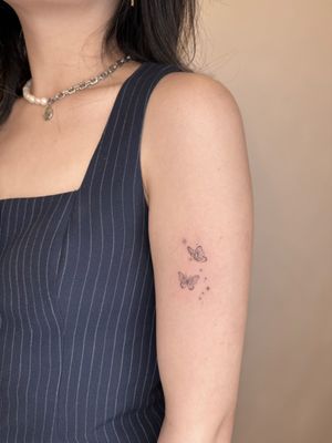 Fine line tattoo by Winnie Shwe featuring a delicate butterfly surrounded by sparkles.