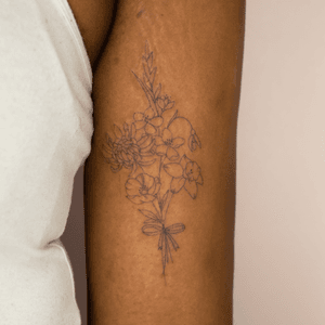 Beautiful fine line flower bouquet on dark skin by Mika Tattoos. Intricate and elegant design.