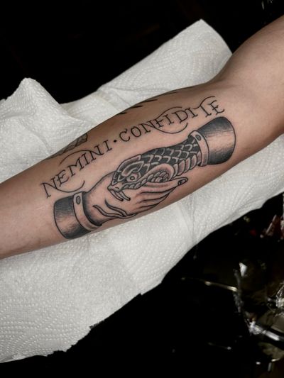 A black and gray tattoo featuring a traditional style snake wrapped around a hand, done by Barney Coles. Small lettering adds detail to this intricate design.