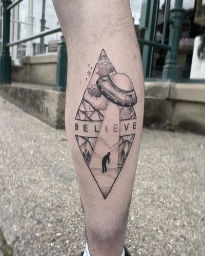 Capture the mystery and wonder of extraterrestrial encounters with this black and gray illustrative tattoo featuring mountains, a UFO, and an alien by Anggi Kokovikas.