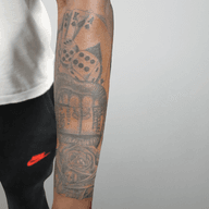 This tattoo is a detailed grayscale composition featuring a combination of gambling and floral elements. The style appears to be photorealistic, with a focus on shading and texture to create depth. The tattoo includes dice, playing cards, a mouth with currency and a rose, giving a dramatic feel.