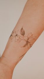 A delicately shaded fine-line floral bracelet wrapped around the forearm, featuring magnolia and nutmeg flowers, drawn freehand to complement the body's lines.