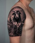 A powerful black and grey realism bull tattoo, representing strength, resilience, and unwavering presence. The composition focuses on anatomical accuracy, textured skin, and controlled contrast, giving the bull a grounded, commanding stance within its natural environment. Tattoo by Roudolf Dimov, London.