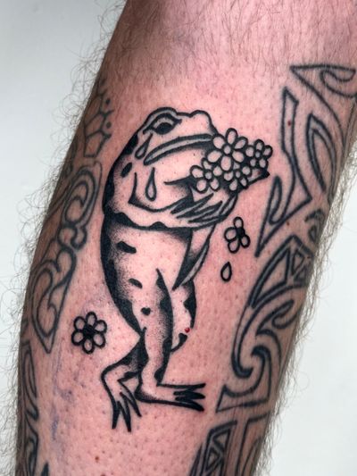 A classic tattoo of a frog in traditional style, created by artist Clara Colibri. The design captures the beauty and essence of this amphibian creature.