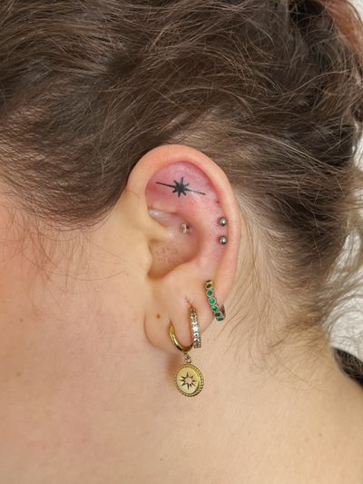 Hand-poked blackwork star tattoo by Laura, located on the ear for a subtle celestial touch.