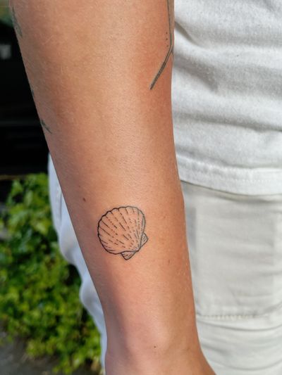 A delicate fine line seashell tattoo, hand-poked with skillful precision by artist Laura. Ignorant style adds unique charm.