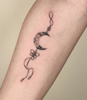 A delicate black and gray micro-realism tattoo by Winnie Shwe featuring a flower with a moon dangle charm design.