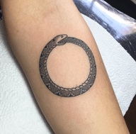 The tattoo presents an ouroboros design, a snake eating its tail forming a circle. The design uses details like dot shading to give texture. The style is simple, and the technique is focused on detail.