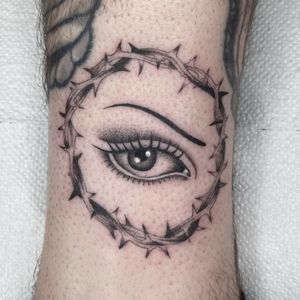 Captivating black and gray illustrative tattoo of an eye entwined with thorns, by artist Megan Foster.