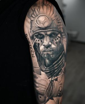 A realistic black and gray tattoo of an Inca, Mayan, or Aztec warrior, skillfully done by Ember.