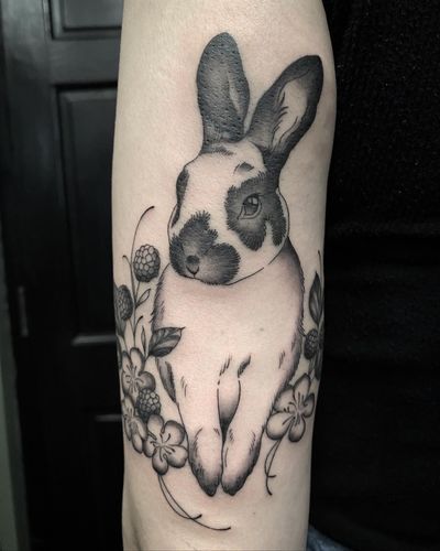 Elegant black and gray illustrative tattoo of a bunny surrounded by delicate flowers, by Amandine Canata.