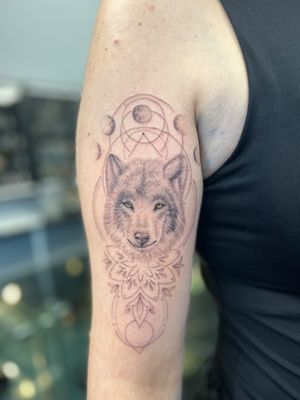 Experience the magic of the moon and the wild spirit of the wolf in this captivating black and gray dotwork tattoo by Ellie Shearer.