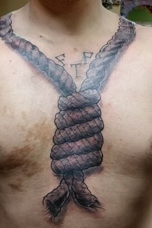 Noose around the collarbone with the knot down the center of the chest. Lettering FTP