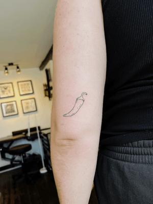 A minimalist fine line hand-poked chilli tattoo done by Laura, capturing the essence of spice in a simple and elegant design.