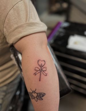 Get a sweet and stylish black and gray fine line illustrative tattoo of a heart, bow, and lollipop from talented artist Sally
