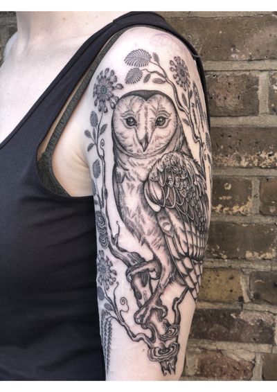 Capture the beauty of nature with this stunning black and gray tattoo by Amandine Canata. Featuring an intricate owl perched on a tree branch with delicate flowers.
