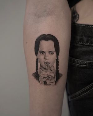 A black-and-gray micro realism tattoo of Wednesday Adams, by artist Kenny Go. Detailed and lifelike portrait of the iconic character.