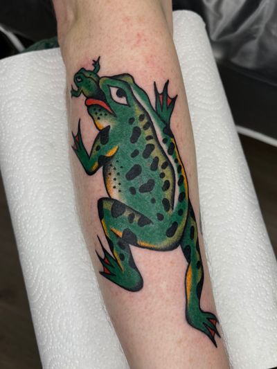 A classic tattoo of a frog, done in traditional style by artist Clara Colibri. Bold outlines and vibrant colors bring this amphibian to life.