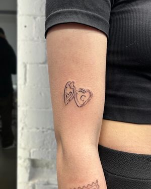 Illustrative tattoo by Ellie Shearer featuring a detailed heart-shaped locket pendant design created in a woodcut style.