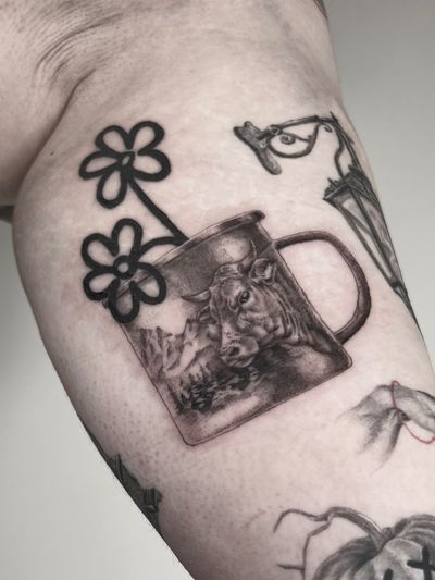 Ignorant-style black and gray tattoo by Lauren featuring a serene mountain landscape with a cow, flower, and mug.