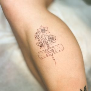 A delicate tattoo featuring a flower, band aid, and bouquet with small lettering of a name. Intricate fine line work by artist Larissa.