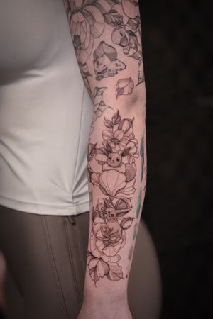A stunning black and gray tattoo featuring Bulbasaur, Eevee, and Espeon in a delicate floral design by Steffan Eagle.