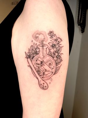 Unique black and gray tattoo combining a frog, flower, potion bottle, and spoon. Expertly done by Michelle Harrison.