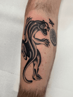 This tattoo features a stylized panther, presented in a traditional tattoo style. The design utilizes heavy black shading to create depth and form, typical of American Traditional tattoos. The panther is depicted in a dynamic pose.