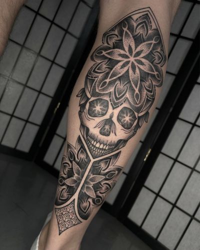 Alice Hope Tattoo combines intricate mandala patterns with a bold skull design in stunning black and gray ink.