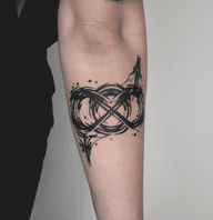 A blackwork tattoo on the forearm depicting a stylized bisexual symbol formed by thick, expressive brushstrokes with splatter details. The design has a raw, artistic feel.