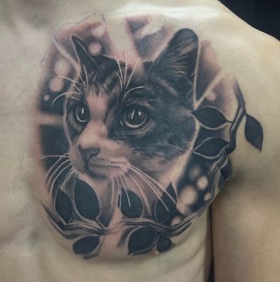 Realistic black and gray tattoo of a cat nestled on a tree branch, capturing the bond between pet and owner.