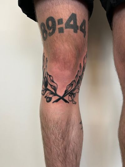 A blackwork and dotwork tattoo of an olive branch plant on the knee, done by Jack Howard.