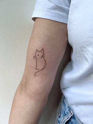 Fine line illustrative tattoo of a delicate cat outline by artist Inna.