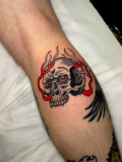 A traditional style tattoo by Barney Coles featuring a skull engulfed in fierce flames.