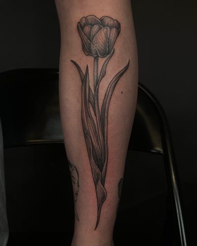 Experience the elegance of a black and gray tulip tattoo, expertly crafted by Kat Jennings in an illustrative style.