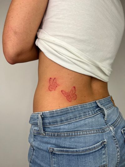 A delicate butterfly in red fine line style, done by artist Emma InkBaby.