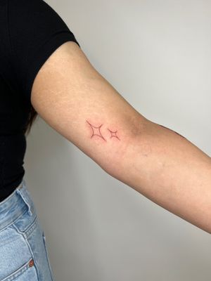 A delicate fine line tattoo by Emma InkBaby, featuring a minimalistic star design with sparkles.