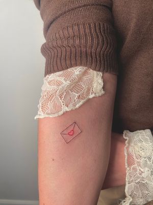 Express your love with this fine line tattoo featuring a heart and letter design, created by talented artist Alina Amberland.